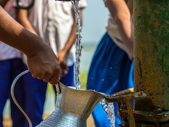 person using outdoor tap to fill water jug in local community